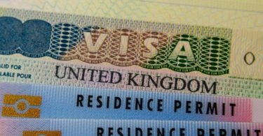 UK BRP cards for Tier 2 work visa placed on top of UK Business VISA sticker in the passport. Close up photo.